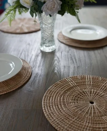 Set of rattan placemats on a large wooden dining table.