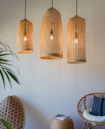 Three tall woven bamboo pendant shades hanging above a rattan chair and ottoman.